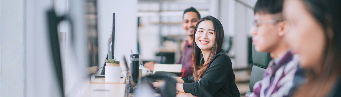 Chinese woman smiling talking to her colleague at her workstation