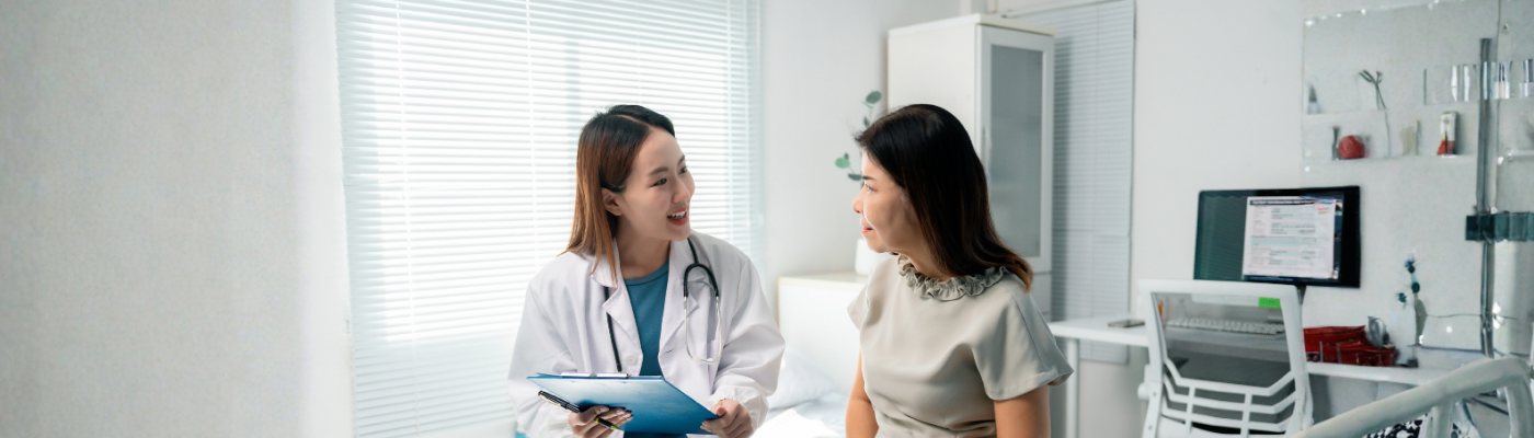 Female physician reviewing medical chart while conversing with seated senior patient