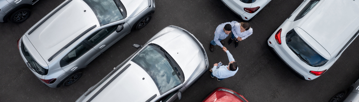 Couple buying a car and closing a deal handshaking with the salesman