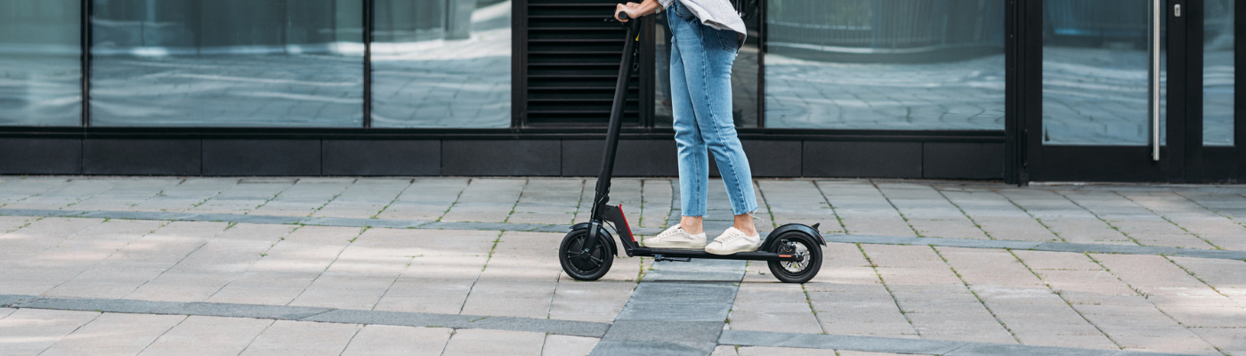 Young businesswoman wearing cycling helmet riding scooter on footpath