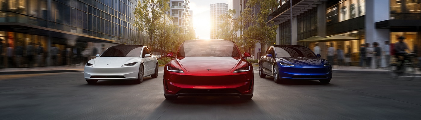三輛白色、紅色及藍色的 Tesla Model 3 電動房車，在日落時分行駛於現代都市街道上。