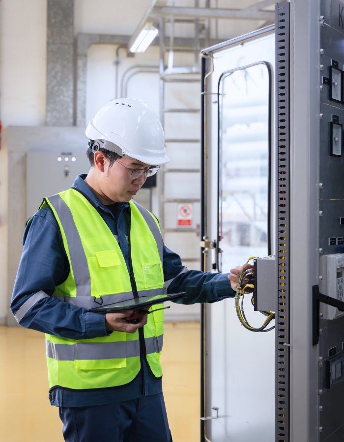 Male engineer in safety helmet and reflective vest inspecting electrical control panel