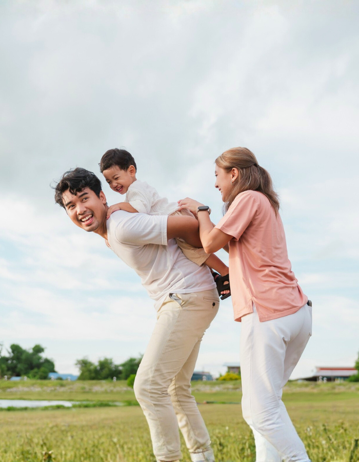 Boy on his father back, while the mother joins in the fun, laughing together
