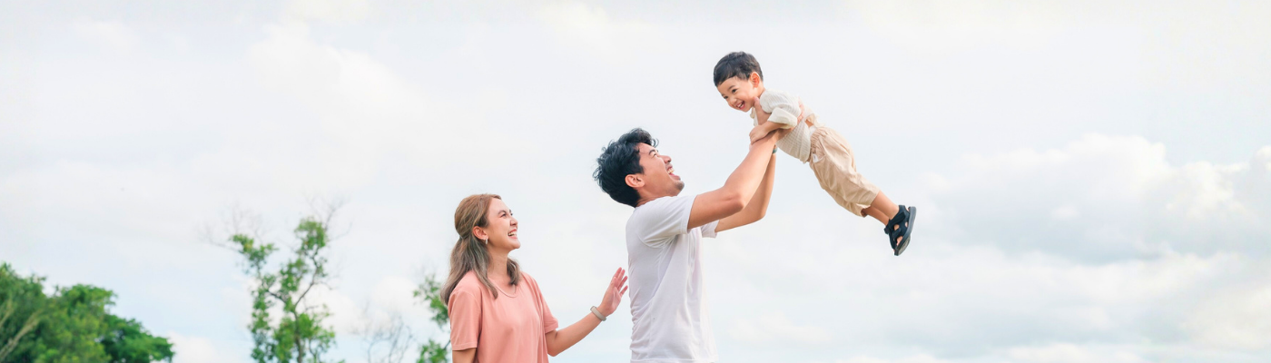 Asian father lifting son up with mother joining in the fun