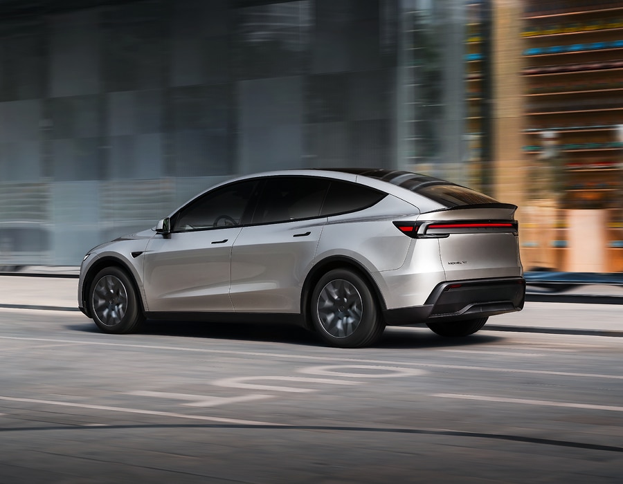 銀色 Tesla Model Y 電動 SUV 行駛於現代都市街道上，從車輛後側方拍攝。