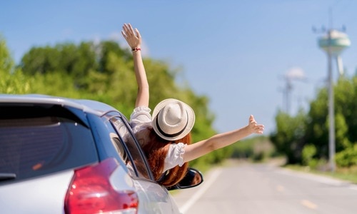 Happy young woman enjoying a summer road trip while traveling on a bright sunny day.